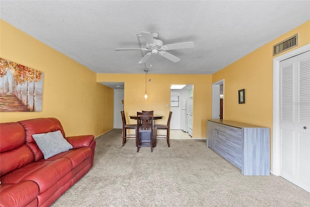 living area featuring light carpet, a textured ceiling, visible vents, and a ceiling fan