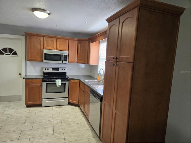 kitchen with brown cabinets, dark countertops, backsplash, appliances with stainless steel finishes, and a sink