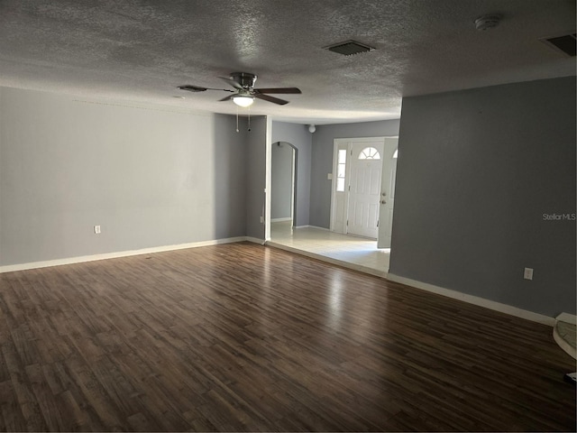 unfurnished room featuring a textured ceiling, visible vents, a ceiling fan, baseboards, and dark wood finished floors