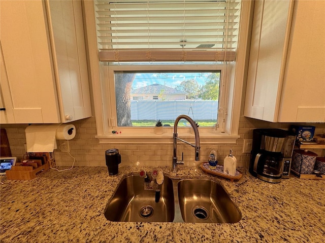 kitchen featuring light stone counters, white cabinets, a sink, and tasteful backsplash