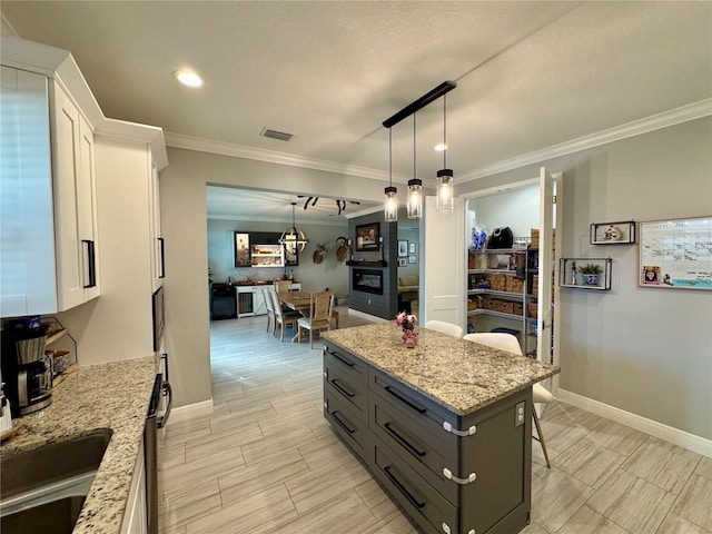 kitchen with light stone counters, a breakfast bar, visible vents, white cabinets, and decorative light fixtures