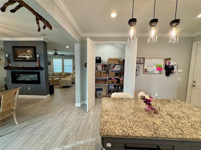 kitchen with a large fireplace, light stone counters, crown molding, and pendant lighting