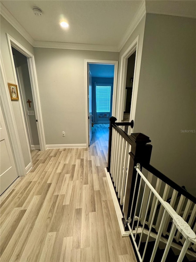 corridor featuring baseboards, ornamental molding, an upstairs landing, and light wood-style floors