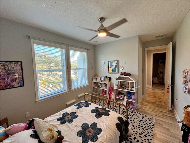 bedroom with visible vents, a ceiling fan, a textured ceiling, light wood-type flooring, and baseboards