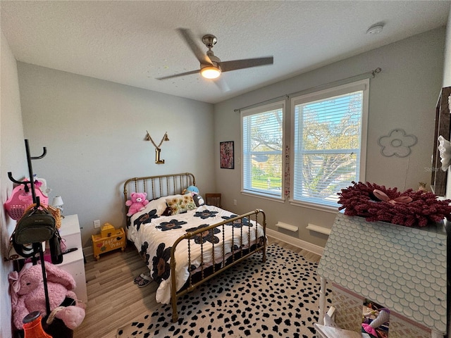 bedroom with light wood-style floors, ceiling fan, baseboards, and a textured ceiling