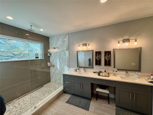 bathroom with a textured ceiling, double vanity, walk in shower, and a sink