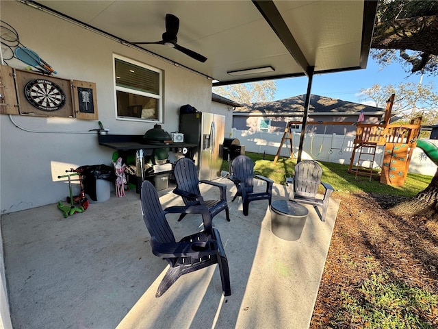 view of patio / terrace featuring a ceiling fan, fence, and a playground