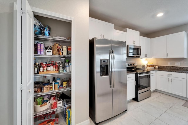 kitchen featuring appliances with stainless steel finishes, white cabinets, dark stone countertops, and light tile patterned floors