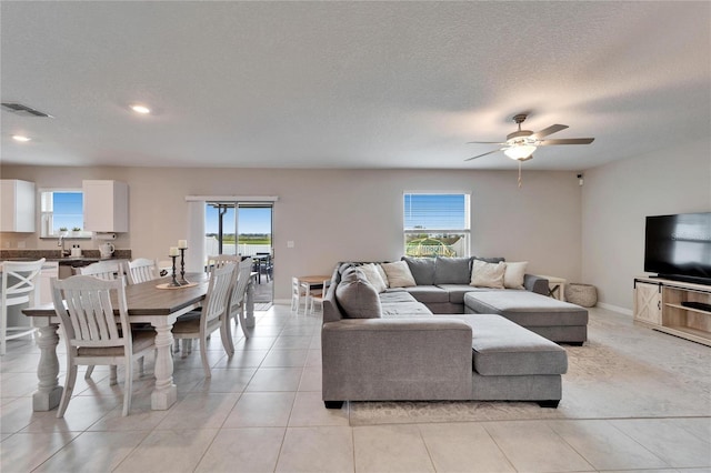 living room featuring visible vents, light tile patterned flooring, ceiling fan, a textured ceiling, and baseboards