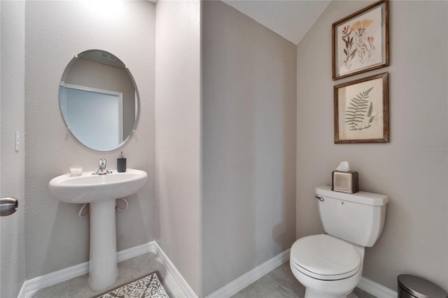 half bathroom featuring baseboards, vaulted ceiling, toilet, and tile patterned floors