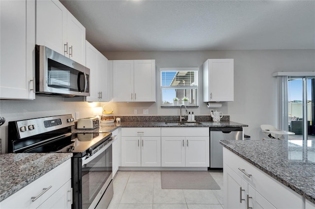 kitchen with white cabinetry, appliances with stainless steel finishes, dark stone counters, and a sink