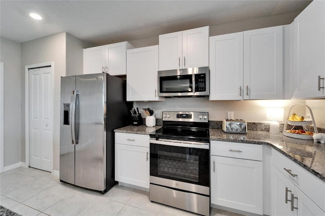 kitchen with light tile patterned flooring, recessed lighting, stainless steel appliances, white cabinetry, and dark stone countertops