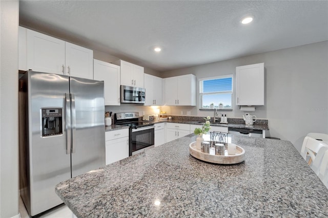 kitchen featuring appliances with stainless steel finishes, a textured ceiling, stone counters, white cabinetry, and a sink