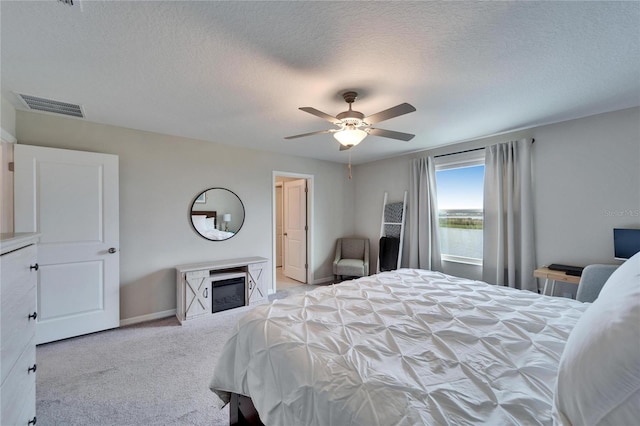 bedroom with baseboards, visible vents, a glass covered fireplace, a textured ceiling, and carpet floors