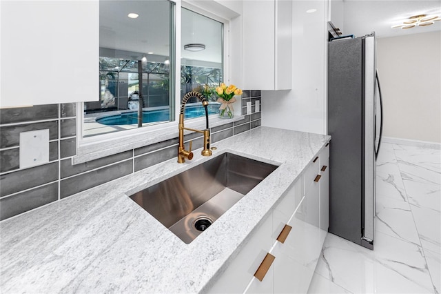 kitchen featuring a sink, white cabinets, marble finish floor, freestanding refrigerator, and light stone countertops