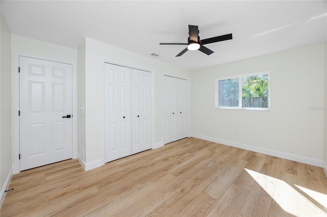 unfurnished bedroom with multiple closets, baseboards, and light wood finished floors