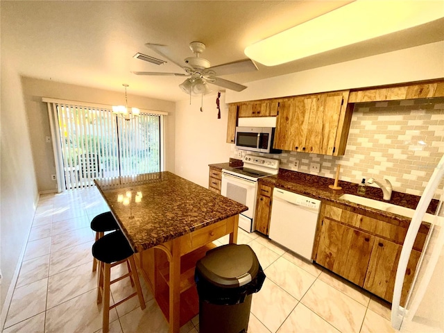 kitchen featuring white appliances, a breakfast bar, visible vents, brown cabinetry, and pendant lighting