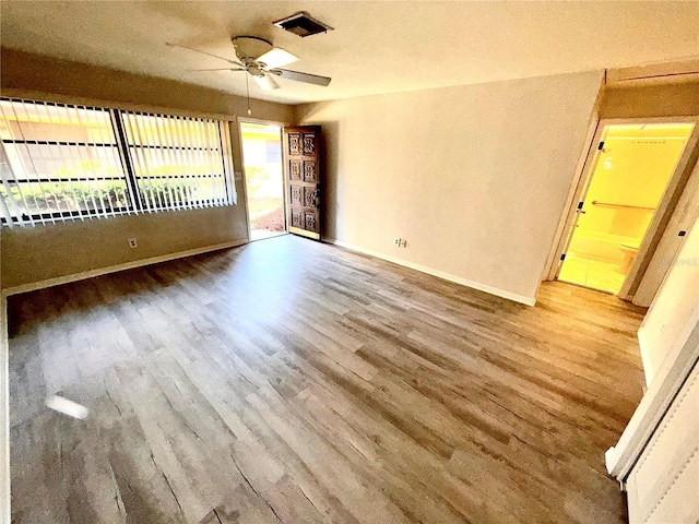 unfurnished room with a ceiling fan, visible vents, baseboards, and wood finished floors