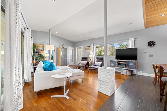 living room featuring lofted ceiling, hardwood / wood-style flooring, a wall unit AC, and baseboards