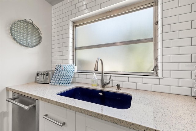 kitchen with decorative backsplash, white cabinetry, a sink, light stone countertops, and dishwasher