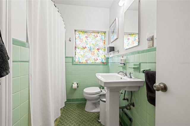 full bath with a shower with curtain, wainscoting, toilet, and tile walls