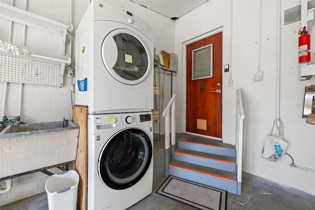 laundry area with concrete block wall, laundry area, a sink, and stacked washing maching and dryer