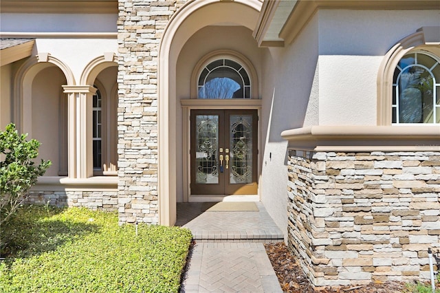 entrance to property with stucco siding, stone siding, and french doors