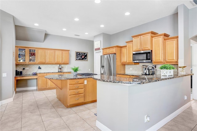 kitchen featuring stainless steel appliances, a peninsula, a center island, dark stone counters, and glass insert cabinets