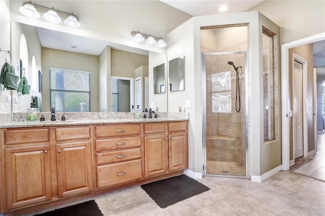 bathroom with double vanity, a stall shower, a sink, tile patterned flooring, and baseboards