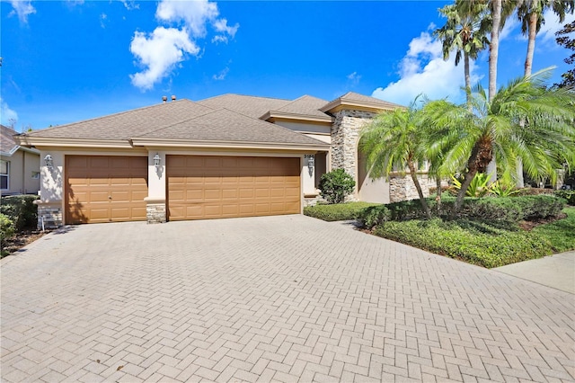 view of front of home featuring decorative driveway, stone siding, a garage, and stucco siding