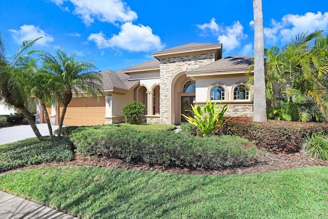 mediterranean / spanish-style house featuring stone siding, driveway, an attached garage, and stucco siding