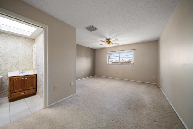 unfurnished room with ceiling fan, a textured ceiling, light carpet, a skylight, and visible vents