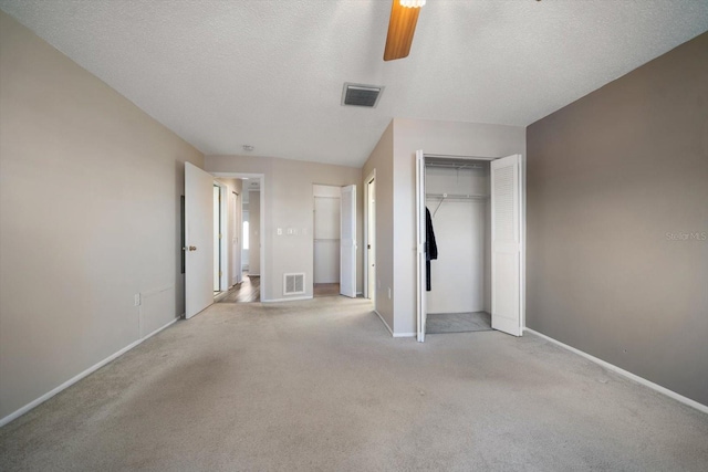 unfurnished bedroom with a textured ceiling, ceiling fan, light carpet, and visible vents