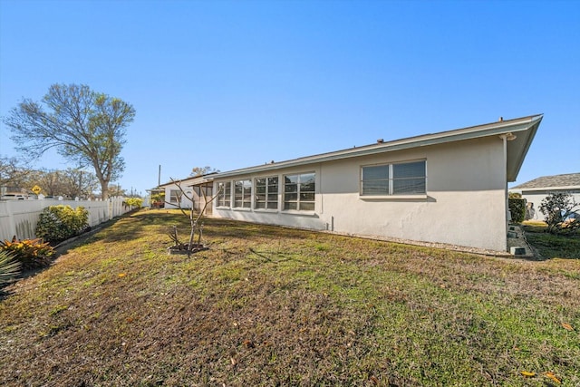 rear view of house featuring a yard, fence, and stucco siding