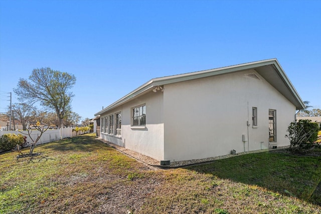 view of home's exterior with a lawn, fence, and stucco siding