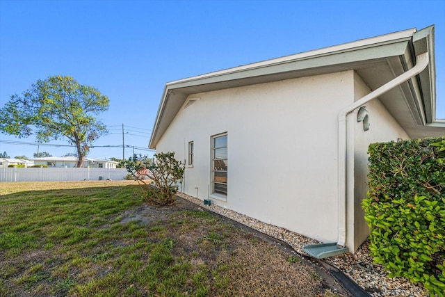 view of side of home with fence, a lawn, and stucco siding