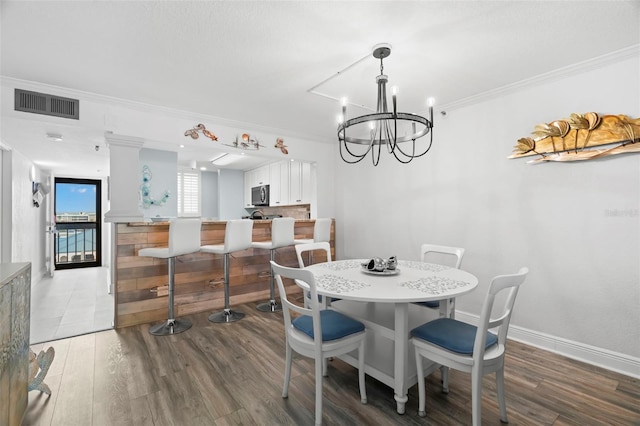 dining area featuring visible vents, ornamental molding, wood finished floors, a chandelier, and baseboards