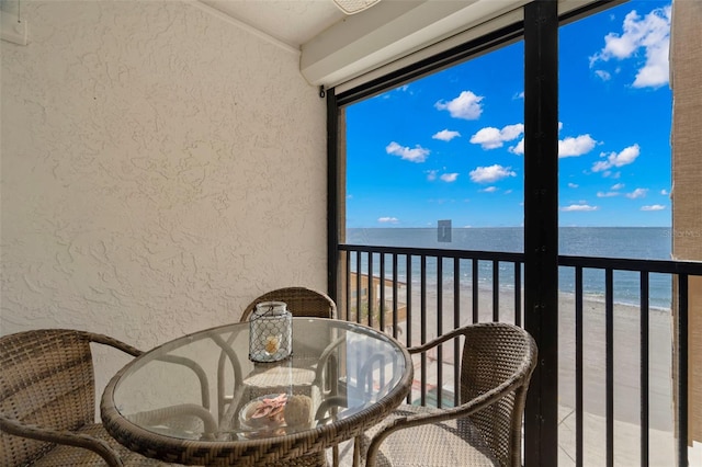 balcony with outdoor dining area, a water view, and a beach view