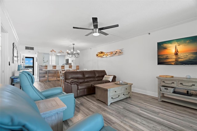 living room featuring light wood finished floors, baseboards, visible vents, crown molding, and ceiling fan with notable chandelier