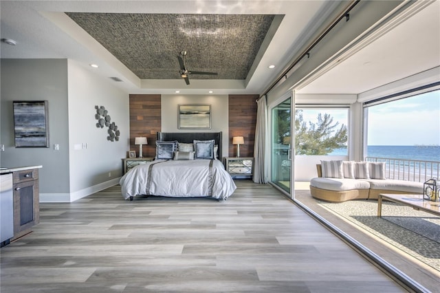 bedroom with a water view, baseboards, light wood-style floors, access to exterior, and a tray ceiling