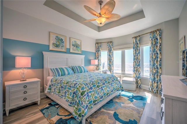 bedroom featuring a tray ceiling, light wood-type flooring, a ceiling fan, and baseboards