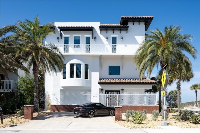 mediterranean / spanish-style house featuring an attached garage, a balcony, a tile roof, driveway, and stucco siding