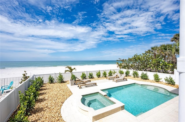 view of swimming pool with a patio, a beach view, a pool with connected hot tub, a water view, and fence