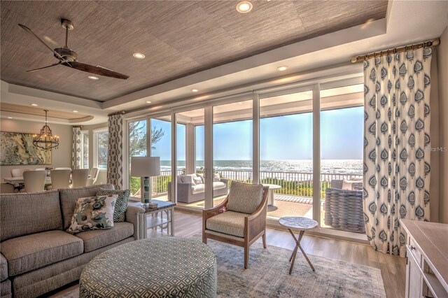 living area with wood ceiling, ceiling fan with notable chandelier, a raised ceiling, and light wood-style flooring