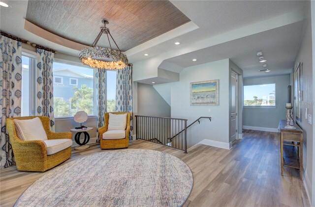 sitting room featuring a raised ceiling, baseboards, an upstairs landing, and wood finished floors