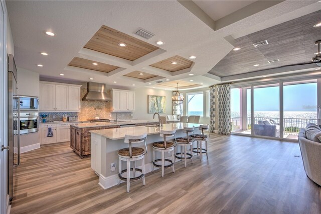 kitchen featuring a breakfast bar, a spacious island, appliances with stainless steel finishes, backsplash, and wall chimney exhaust hood