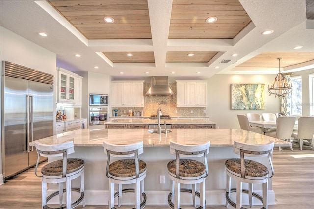 kitchen featuring tasteful backsplash, a spacious island, a sink, built in appliances, and wall chimney exhaust hood