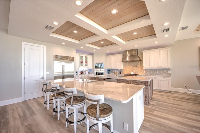 kitchen featuring built in appliances, wall chimney range hood, a spacious island, and visible vents