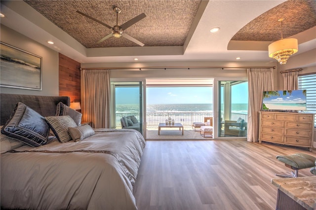 bedroom featuring access to outside, a raised ceiling, wooden walls, and wood finished floors