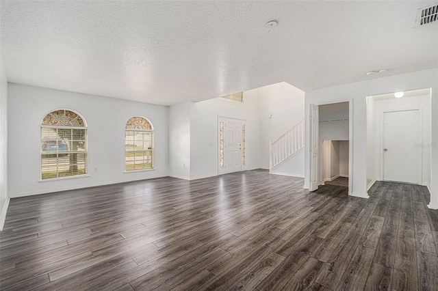 unfurnished living room with a textured ceiling, visible vents, baseboards, stairway, and dark wood-style floors